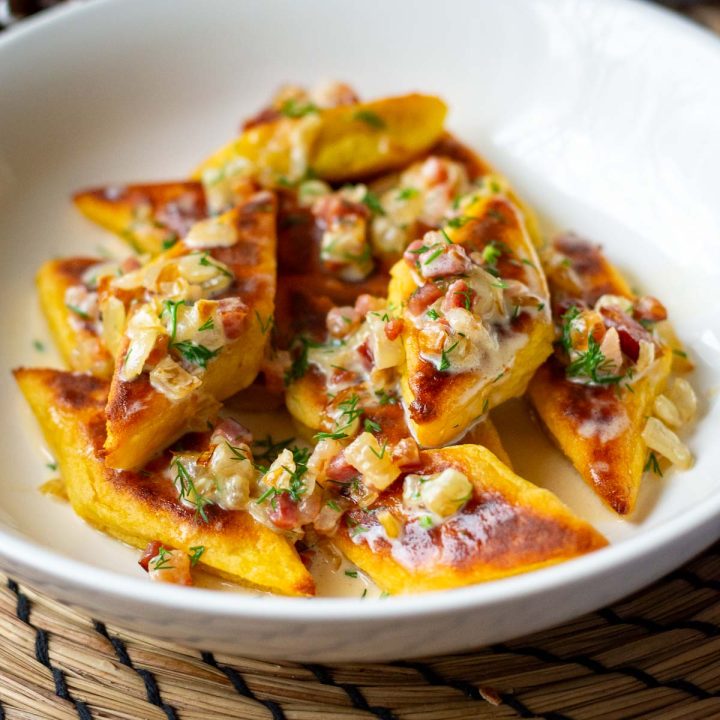 A bowlful of lithuanian potato bites topped with cream and bacon sauce.