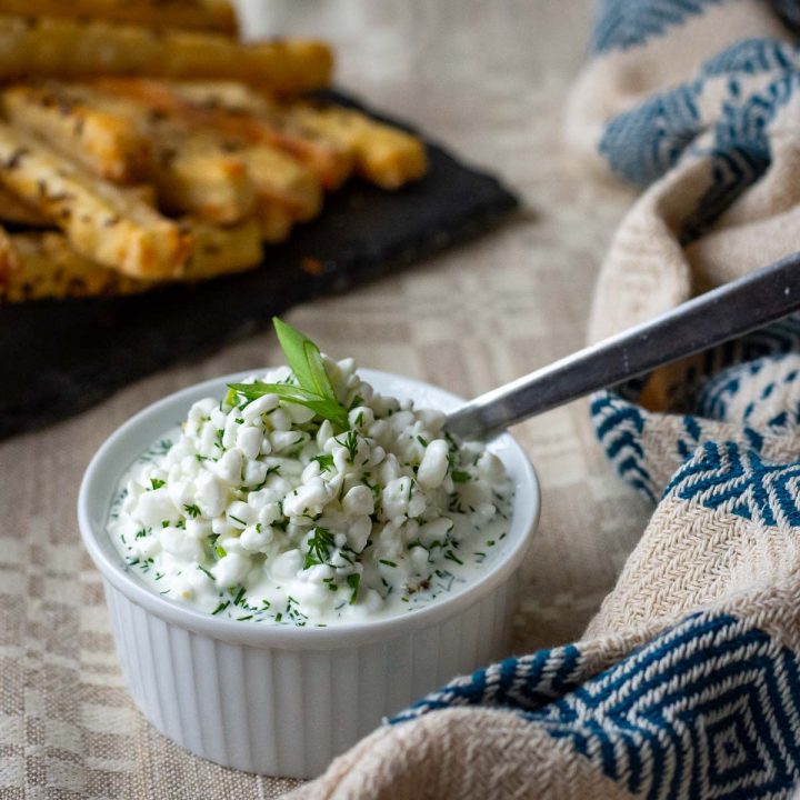 Lithuanian cottage cheese sauce for potato dishes in a small white ramekin with a spoon in it.