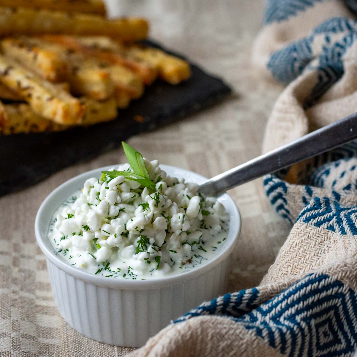 Lithuanian cottage cheese sauce for potato dishes in a small white ramekin with a spoon in it.