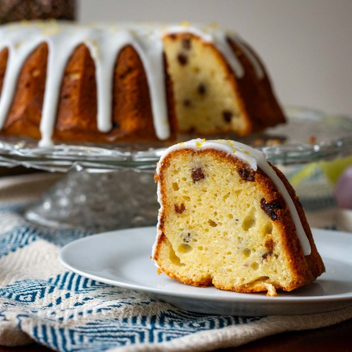A slice of Lithuanian Easter Bundt Cake on a small white plate with the rest of the cake in the background.