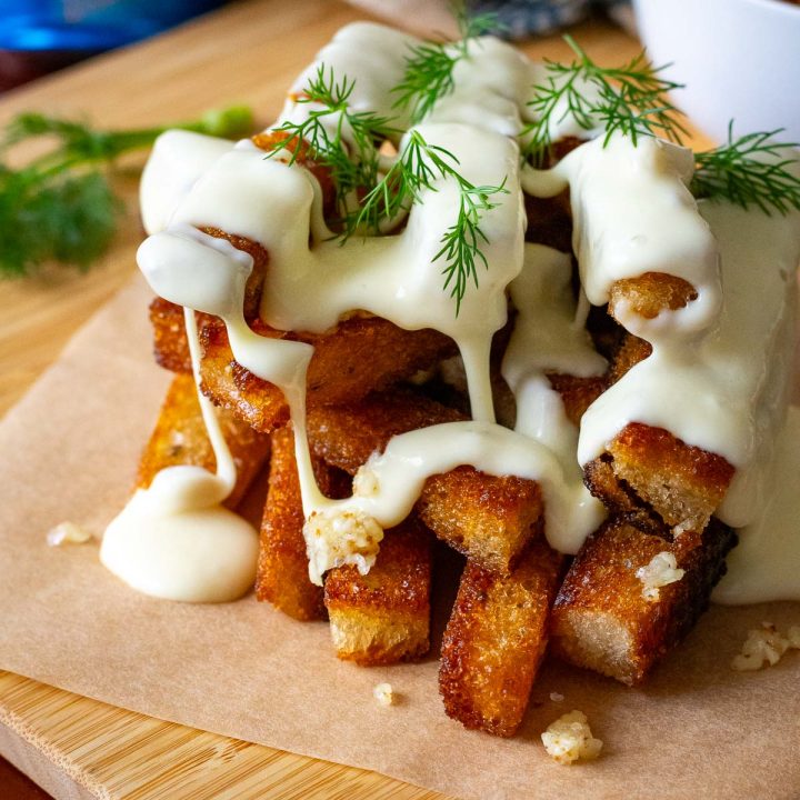 Lithuanian fried bread stacked and topped with cheese sauce on a wooden board.