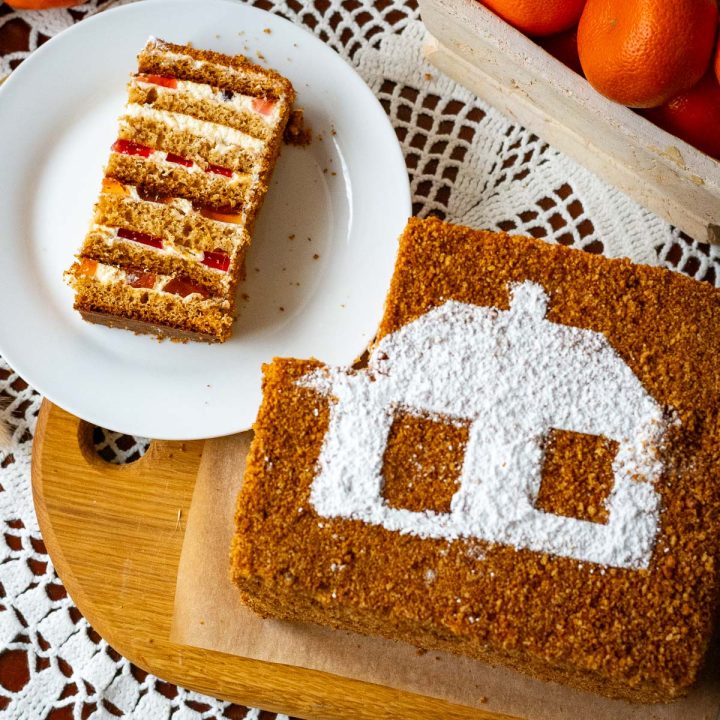 A slice of Lithuanian Honey Sponge cake next to the whole Lithuanian Cake "Sodzius".
