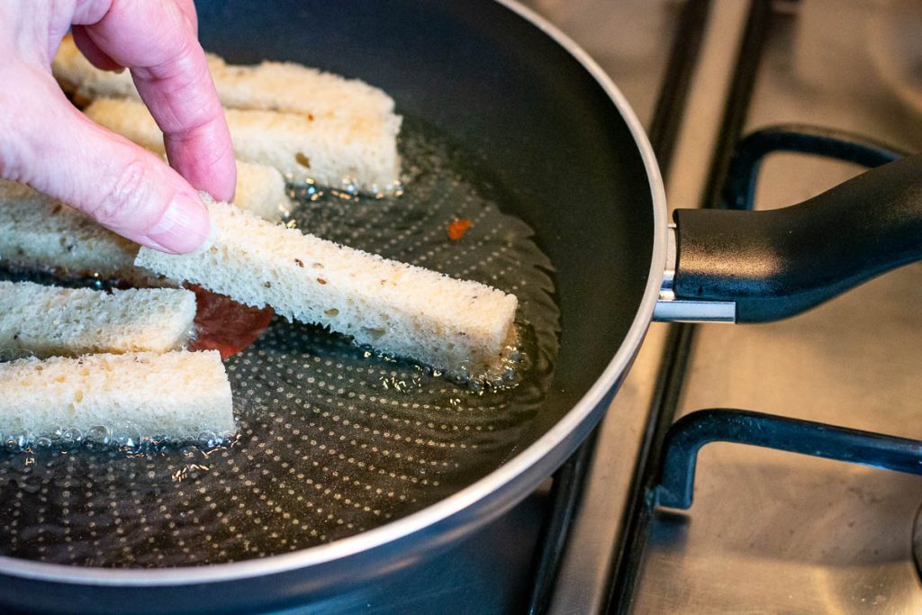 Placing bread sticks in hot oil in a frying pan. 