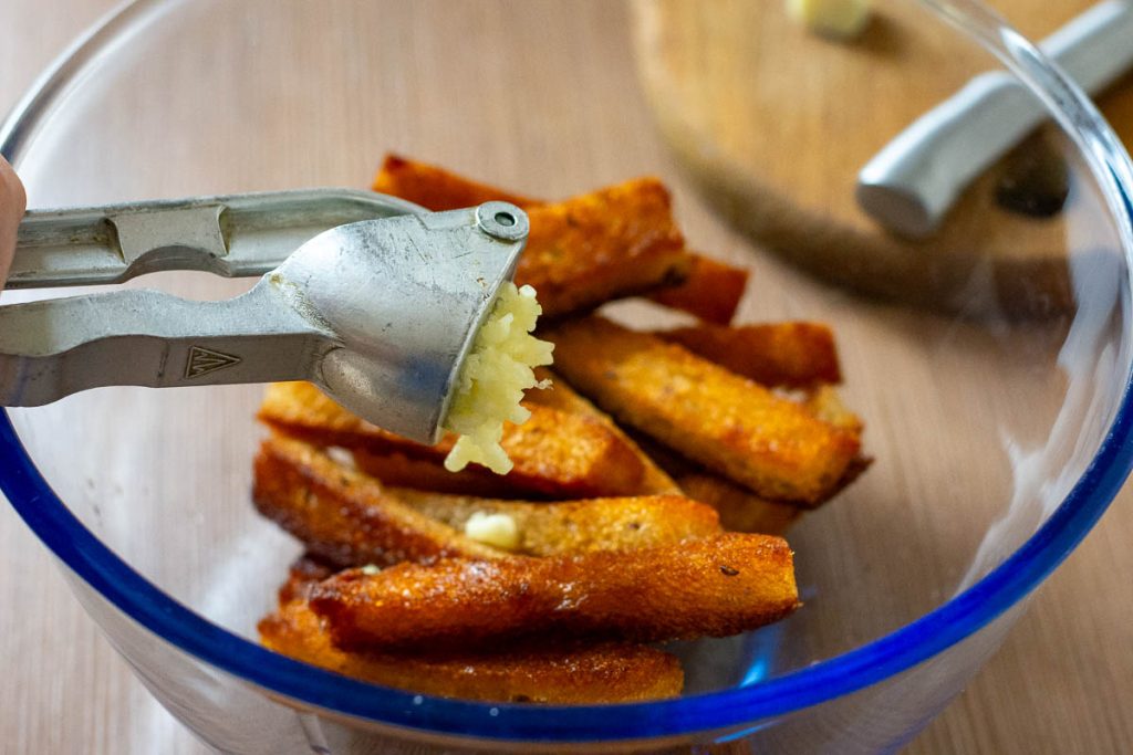 Adding garlic to a bowl with fried bread. 