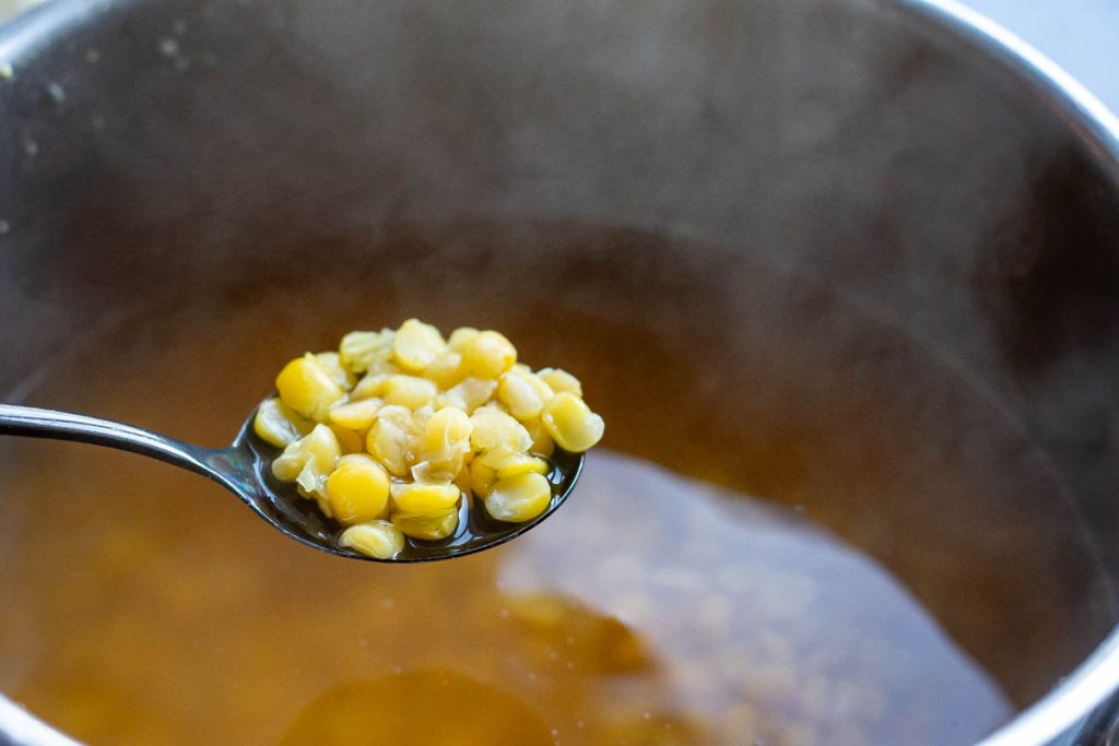 A spoonful of peas liften out of a large pot to check the doneness. 