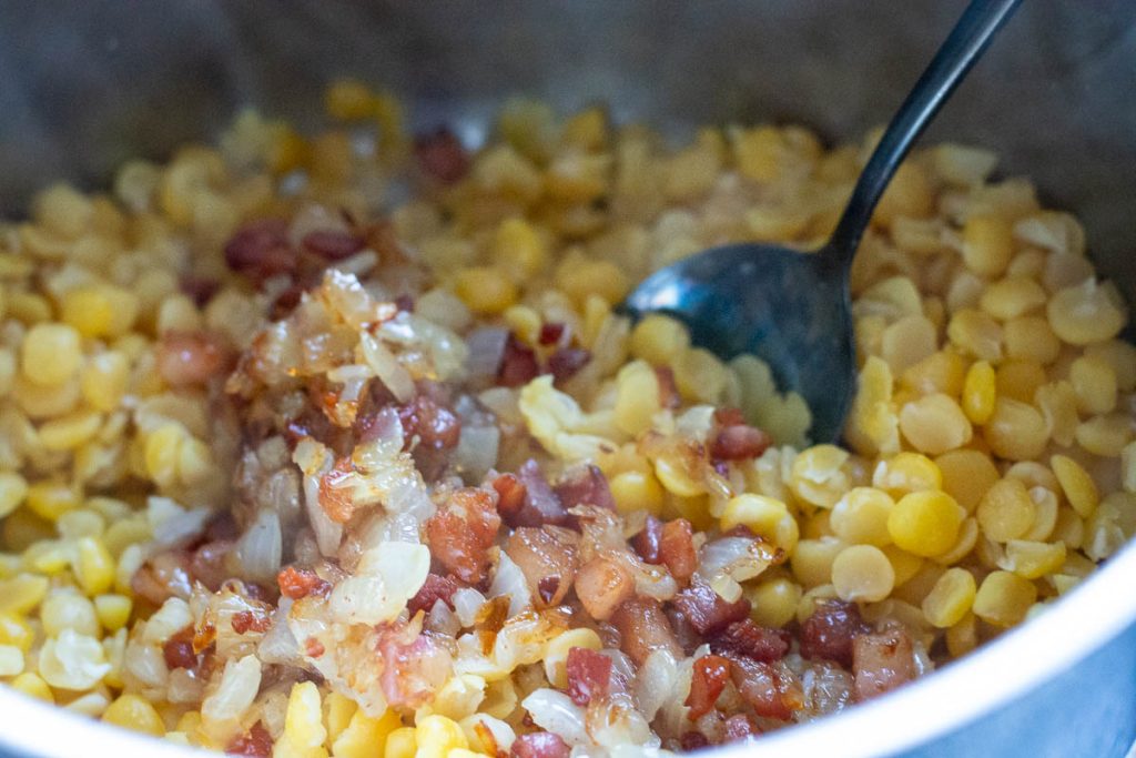 Mixing the onion and bacon mixture with cooked yellow split peas. 
