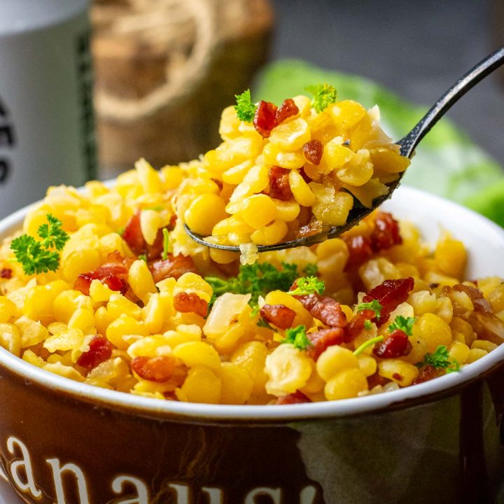 A spoonful of yellow split peas and bacon being take out of a bowl.