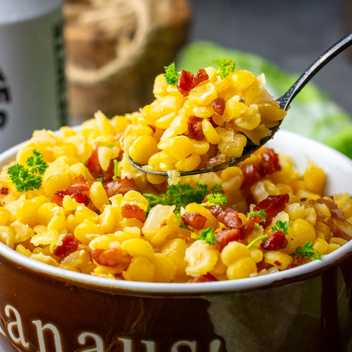 A spoonful of yellow split peas and bacon being take out of a bowl. 