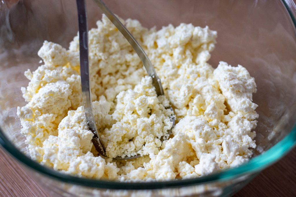 Mashing Lithuanian farmer's cheese with a potato masher to vreak up large curds.