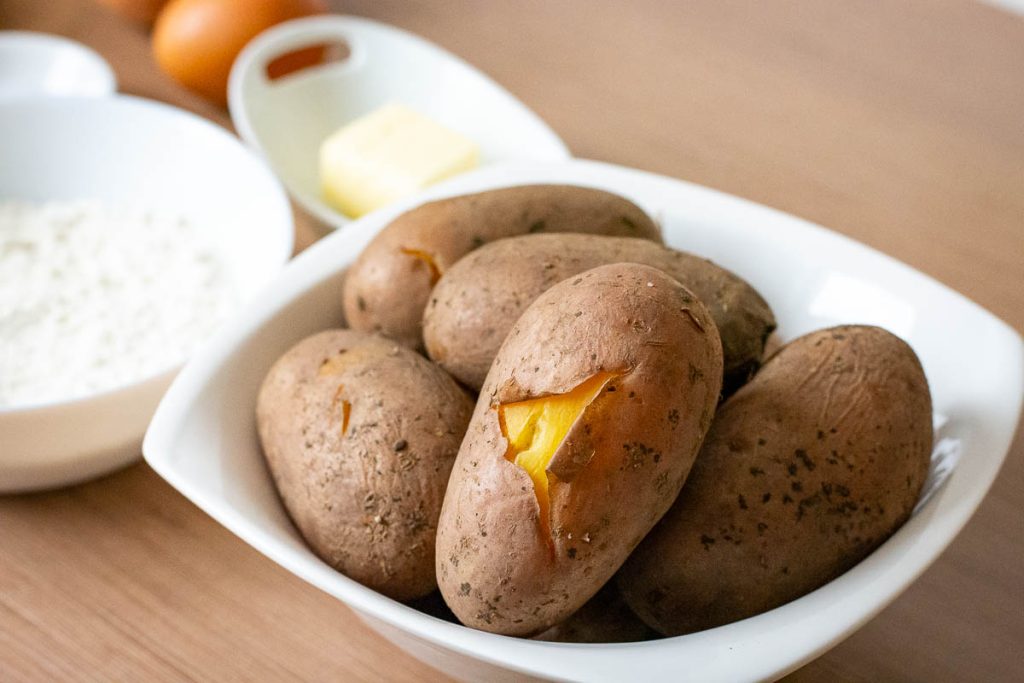 Skin-on yellow-freshed starchy Lithuanian boiled potatoes cooling in a white bowl.