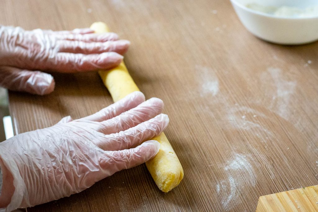 Flattening a rolled rope of pottao dough on a kitchen surface.