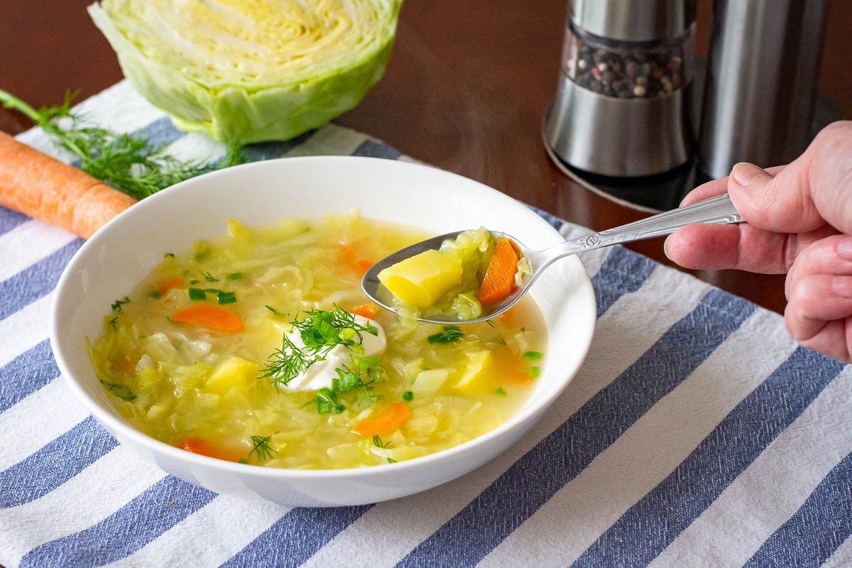 Taking a spoonful of Lithuanian Cabbage Soup from a bowl.
