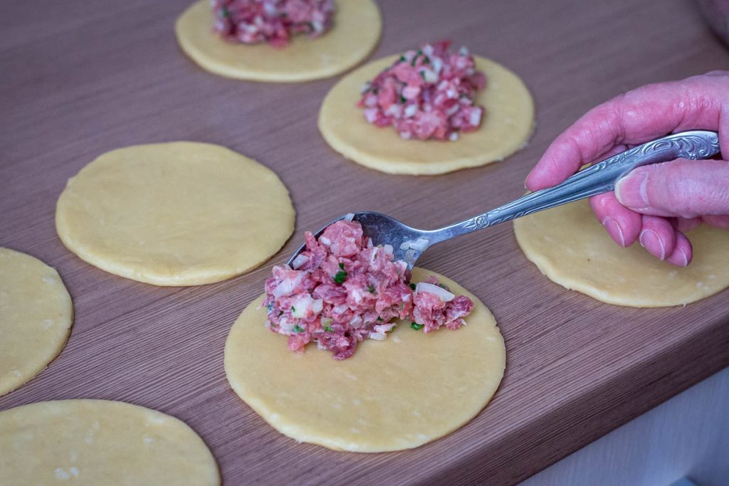 Placing a heaped tablespoon of pork filling onto each pastry circle.