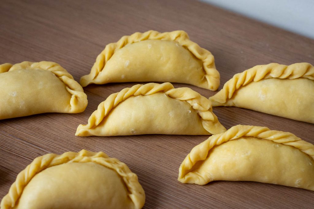 Lithuanian meat pies with crimped pastry edges on a wooden work surface.