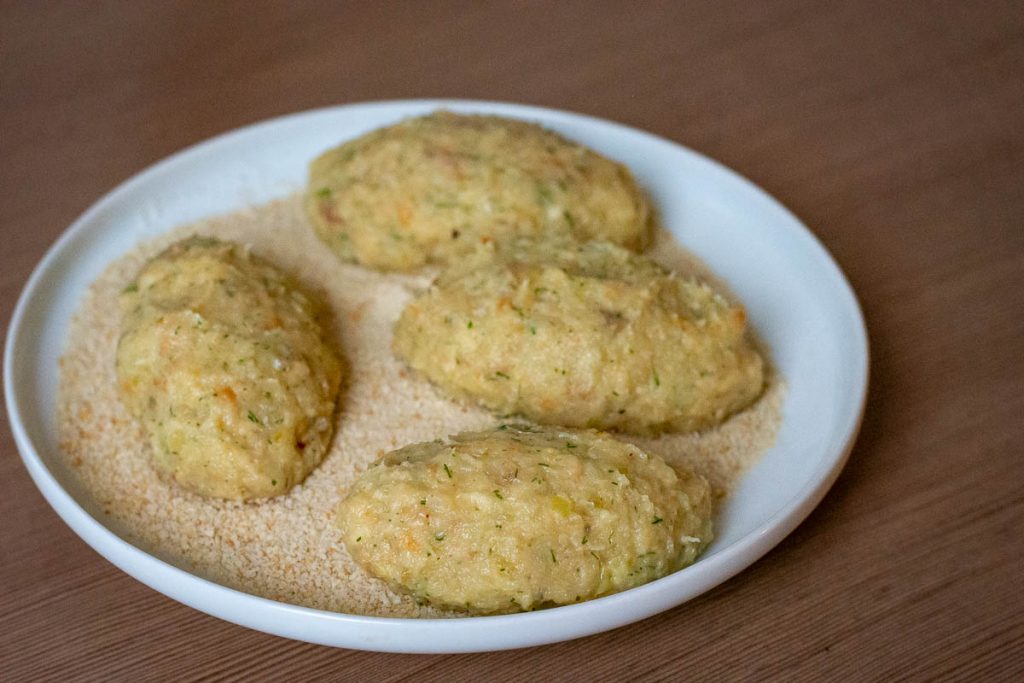 Oblong fish patties on a plate with breadcrumbs.