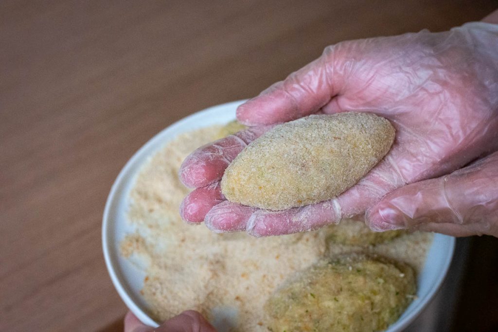 Shaped and breaded Lithuanian fishcake picked up in a gloved hand.