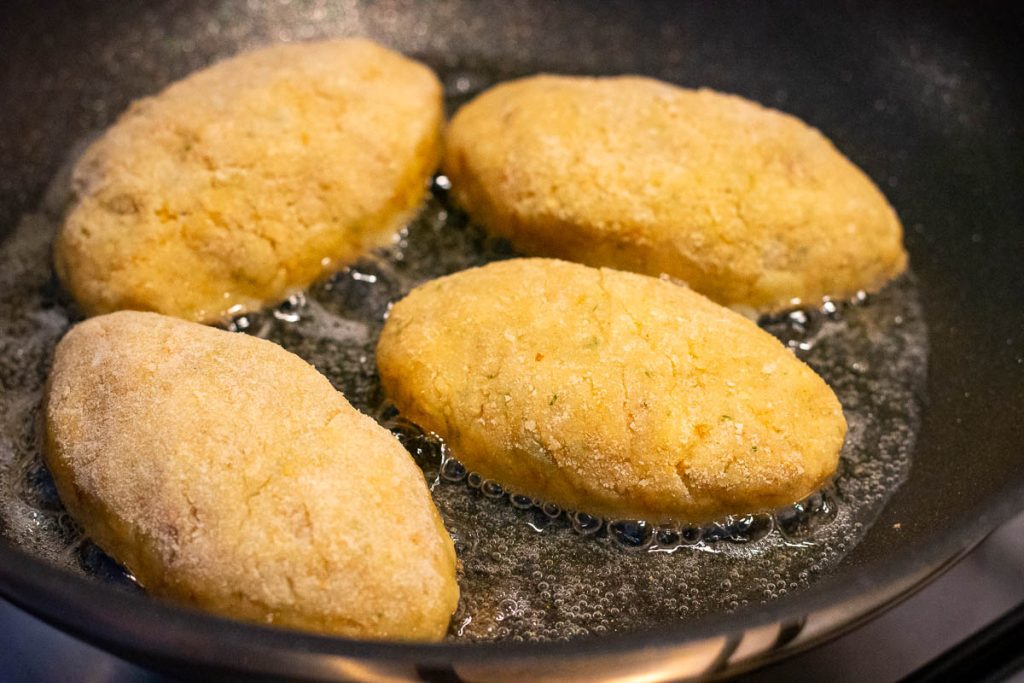 Fishcakes frying in hot oil in a frying pan.