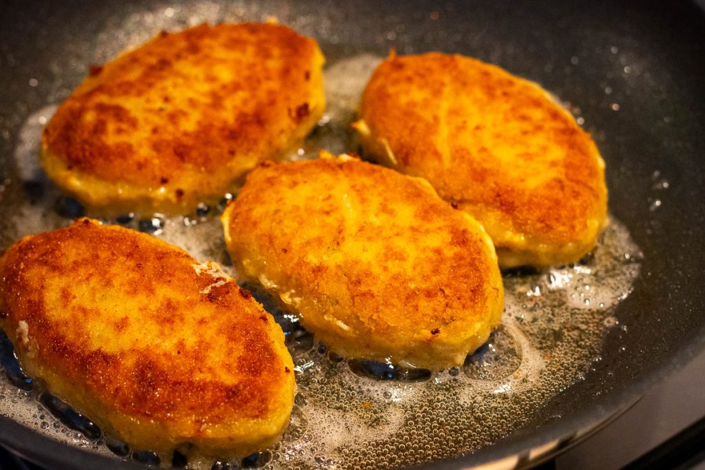 Golden brown Lithuanian fish cakes frying in oil.