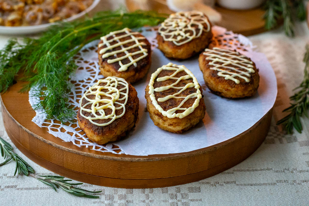Lithuanian fish cakes, known as žuvies kotletai in Lithuanian, with mayonnaise piped on top arranged on awooden serving board.