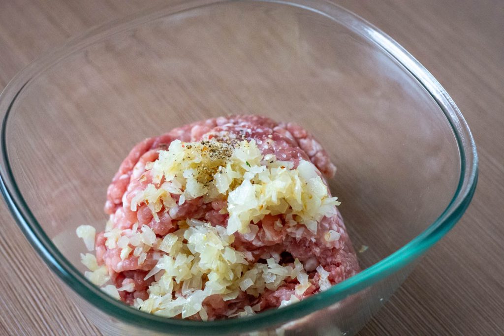Ground pork with sauteed onions in a large glass mixing bowl.