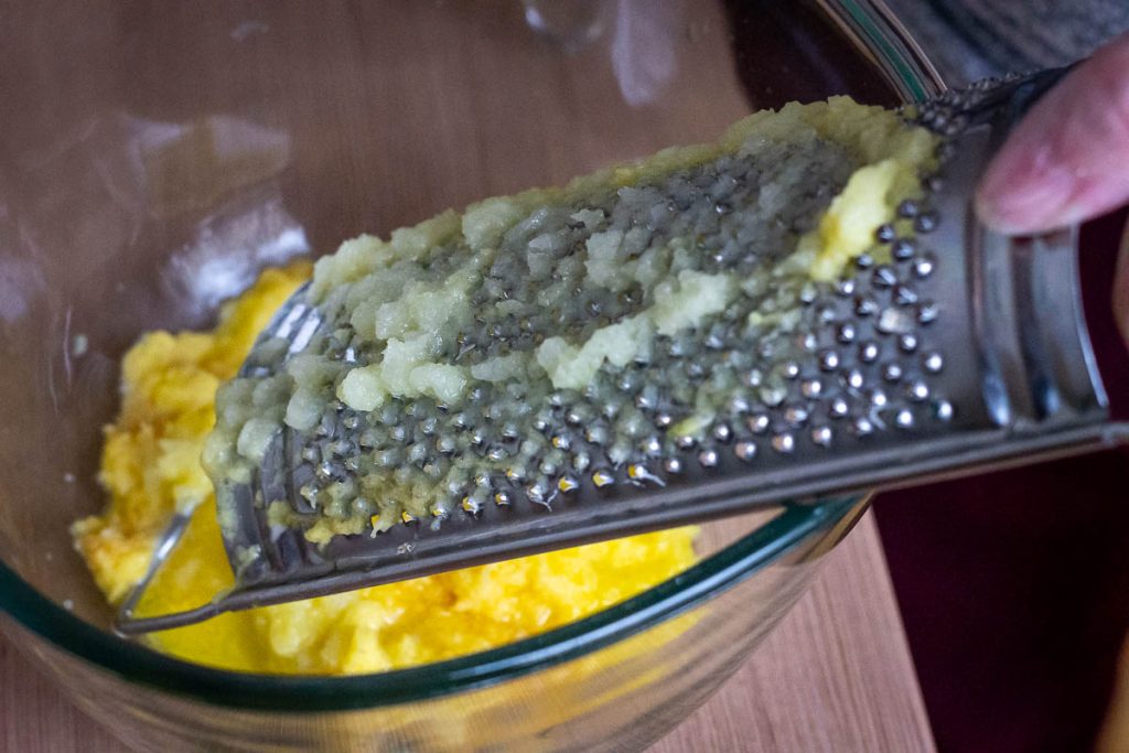 Grating potatoes finely into a glass bowl.