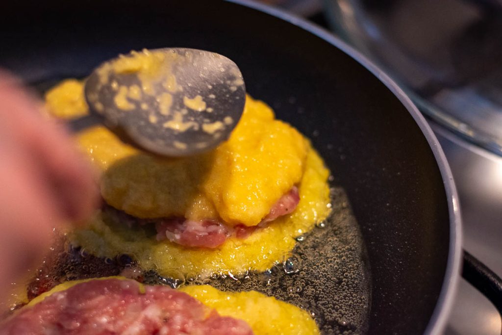 Topping the pork patty with more potato mixture to encase it.