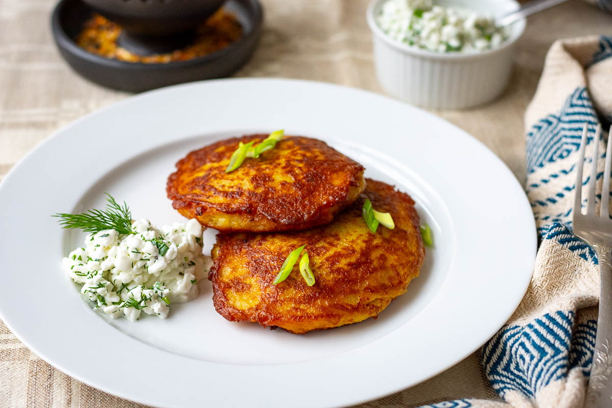 Two Lithuanian Meat Stuffed Potato Pancakes on a white plate served with herby cottage cheese sauce.