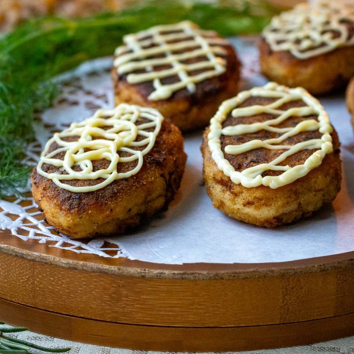 Lithuanian fish cakes, known as žuvies kotletai in Lithuanian, with mayonnaise piped on top arranged on awooden serving board.