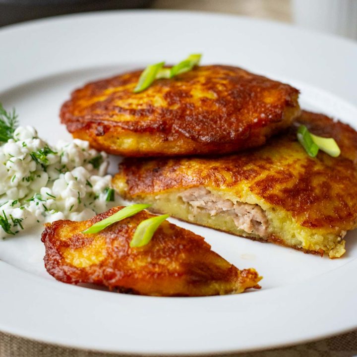 Lithuanian meat stuffed potato pancakes on a white plate served with cottage cheese sauce.