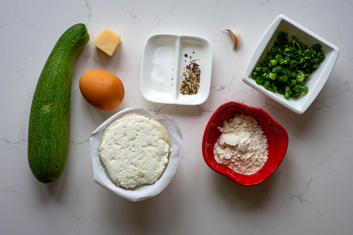 Ingredients for Lithuanian Zucchini pancakes with farmer's cheese on a light kitchen worktop.