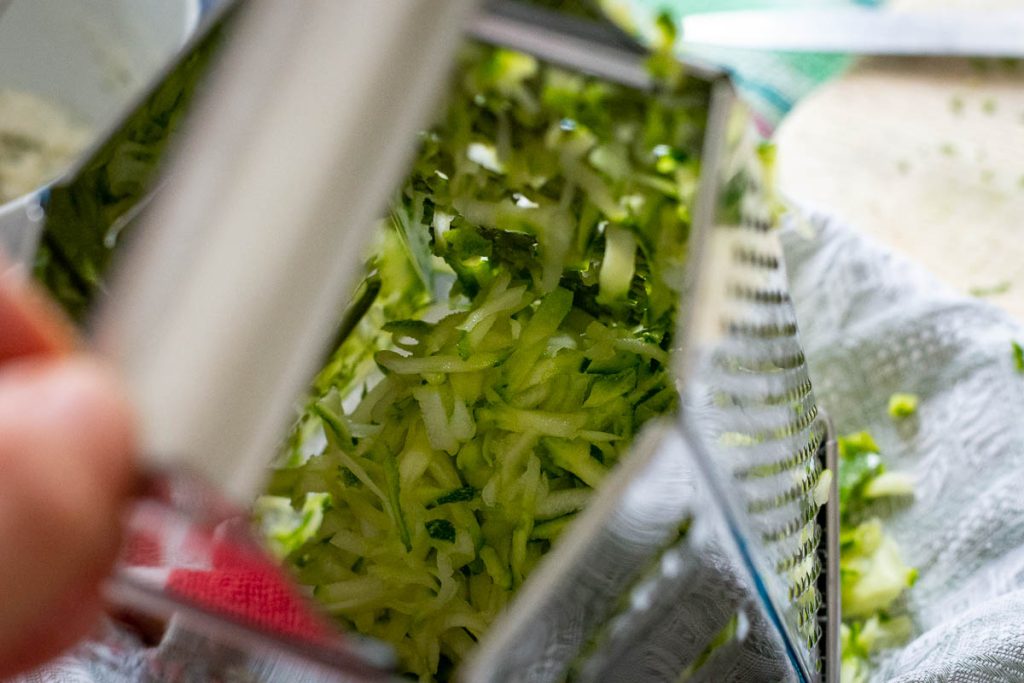 Grating zucchini using a box grater.