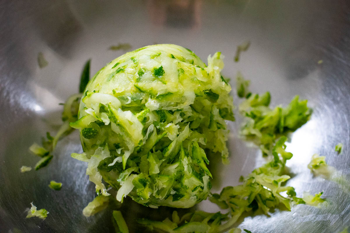 Squeezed out grated zucchini in a metal mixing bowl.
