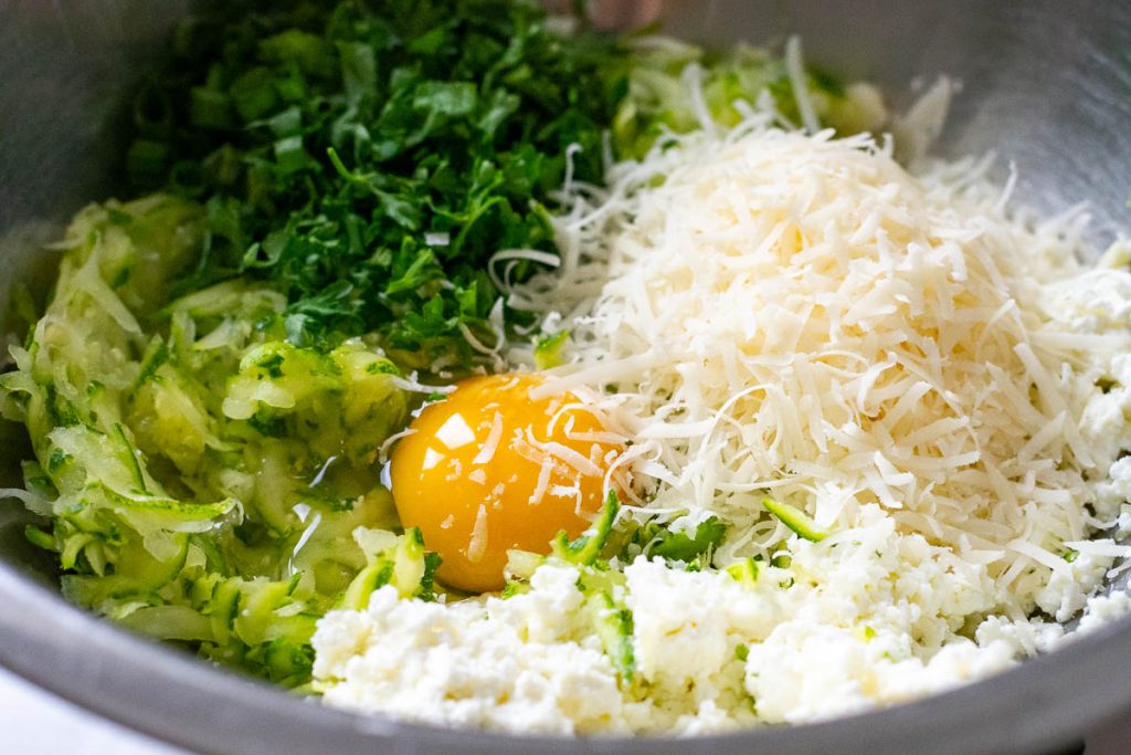 All Lithuanian zucchini fritter ingredients in a large metal mixing bowl.