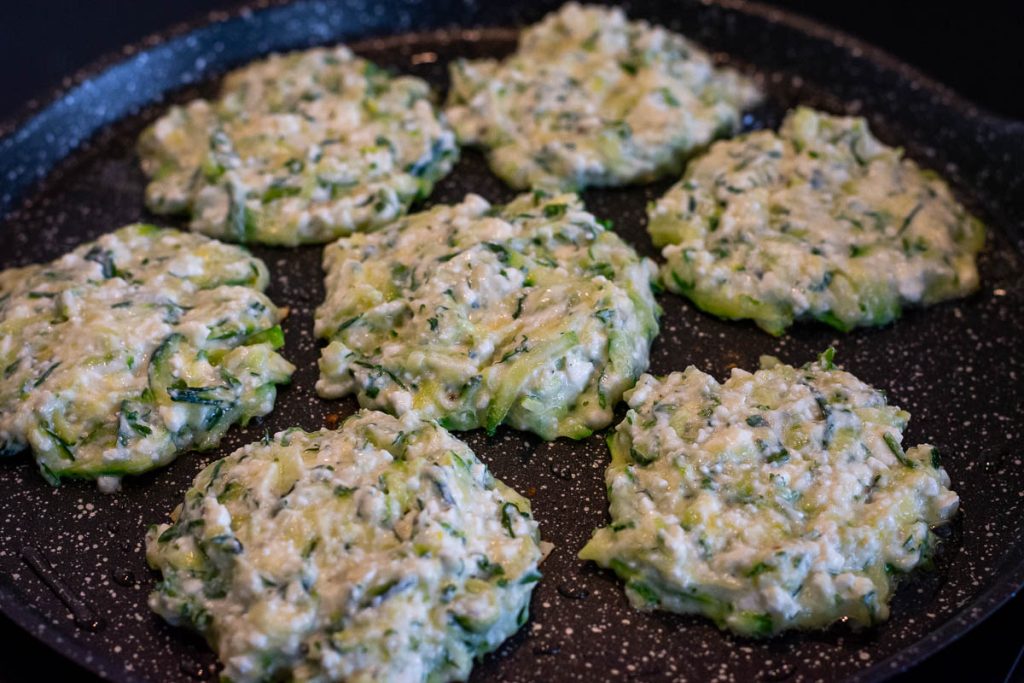 7 zucchini fritters with farmer's cheese in a frying pan.