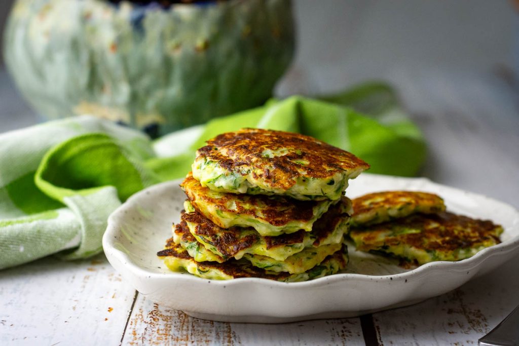 A starck of soft Lithuanain zucchini fritters with farmer's cheese on a small white plate.