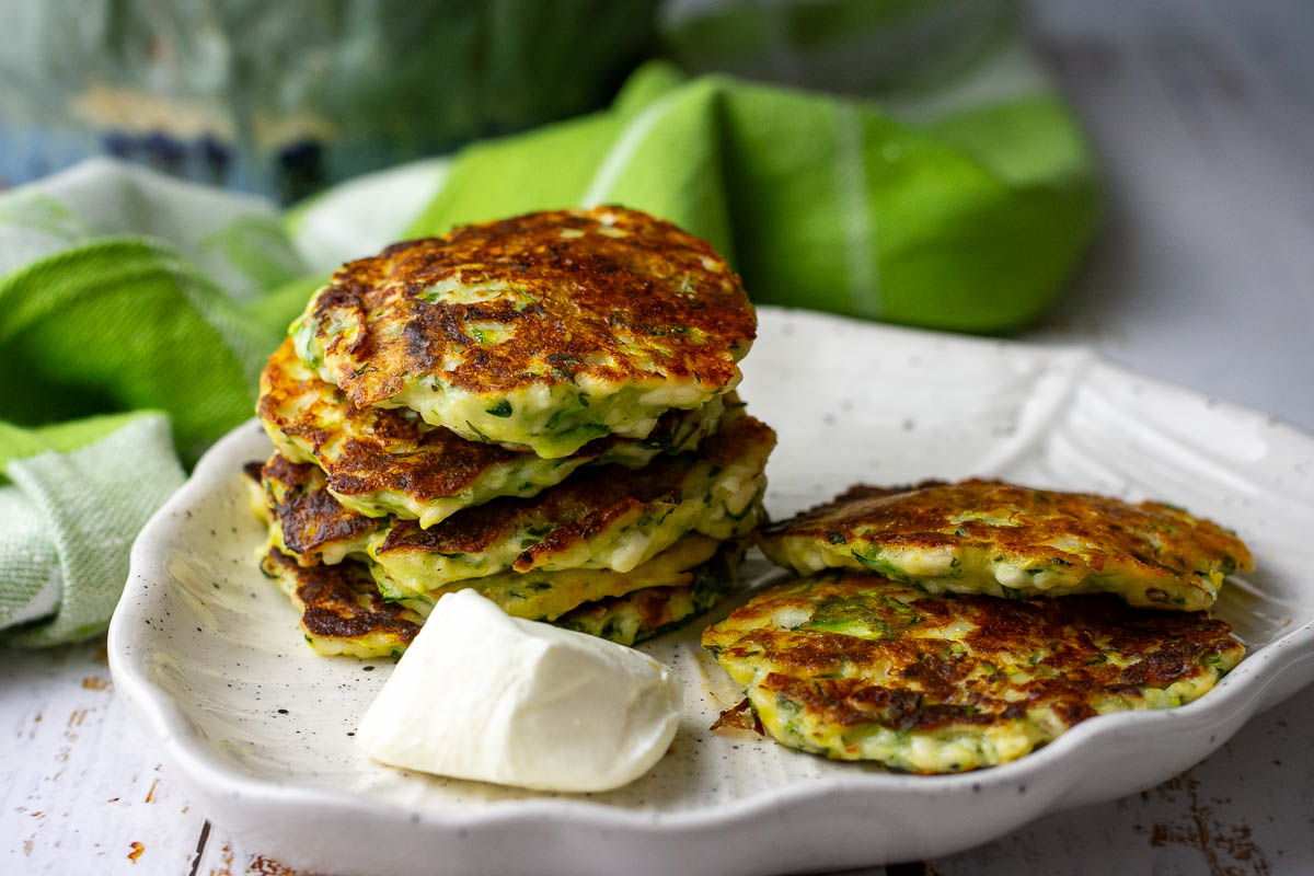 Lithuanian zucchini fritters served with a dollop of sour cream on a white plate.