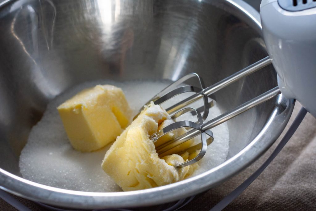 Beaters of electring hand mixer in a bowl with butter and sugar.