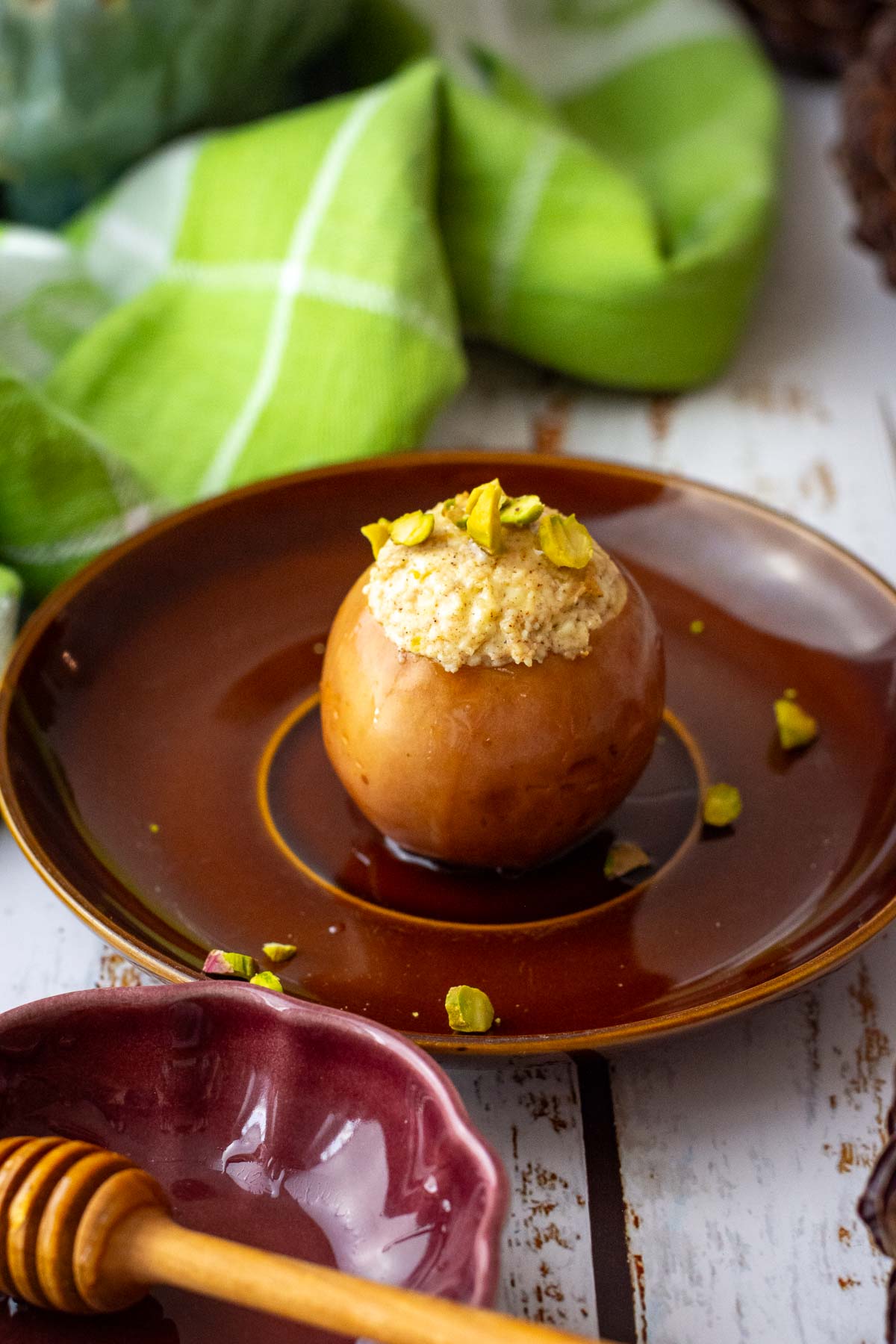 Lithuanian baked apple on a brown plate with honey and chopped pistachios on top.
