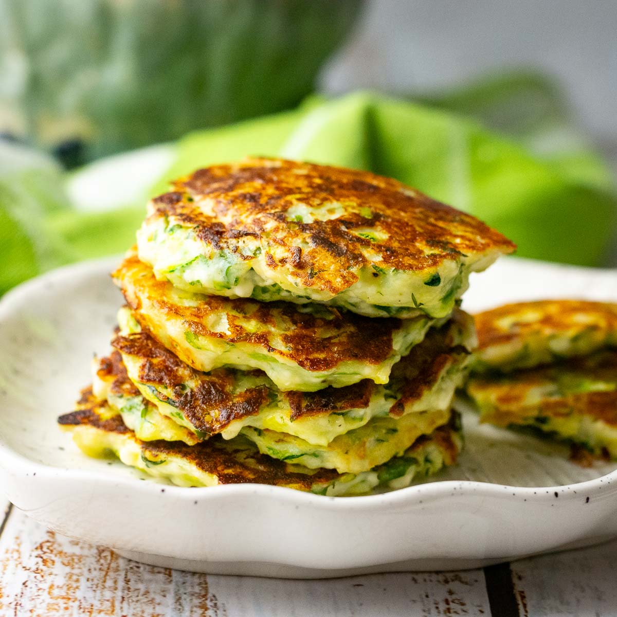A stack of soft Lithuanian Zucchini fritters with farmer's cheese on a white plate.