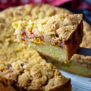 A slice of Lithuanian plum cake with crumb topping being cut and lifted on the end of a knife.