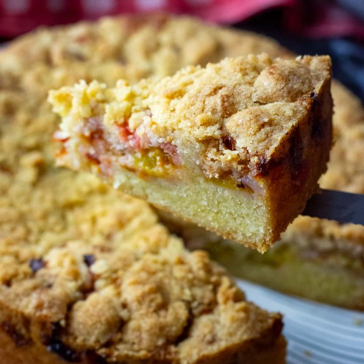 A slice of Lithuanian plum cake with crumb topping being cut and lifted on the end of a knife.