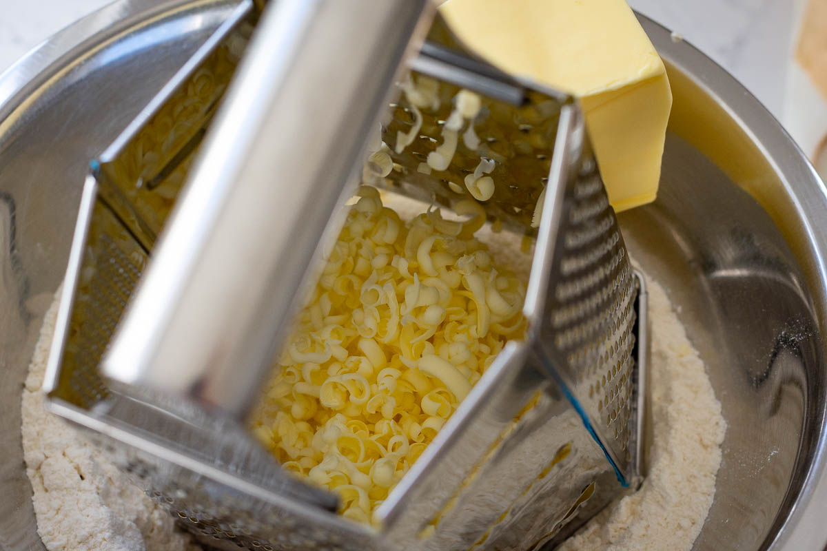 Grating frozen butter using a box grater.