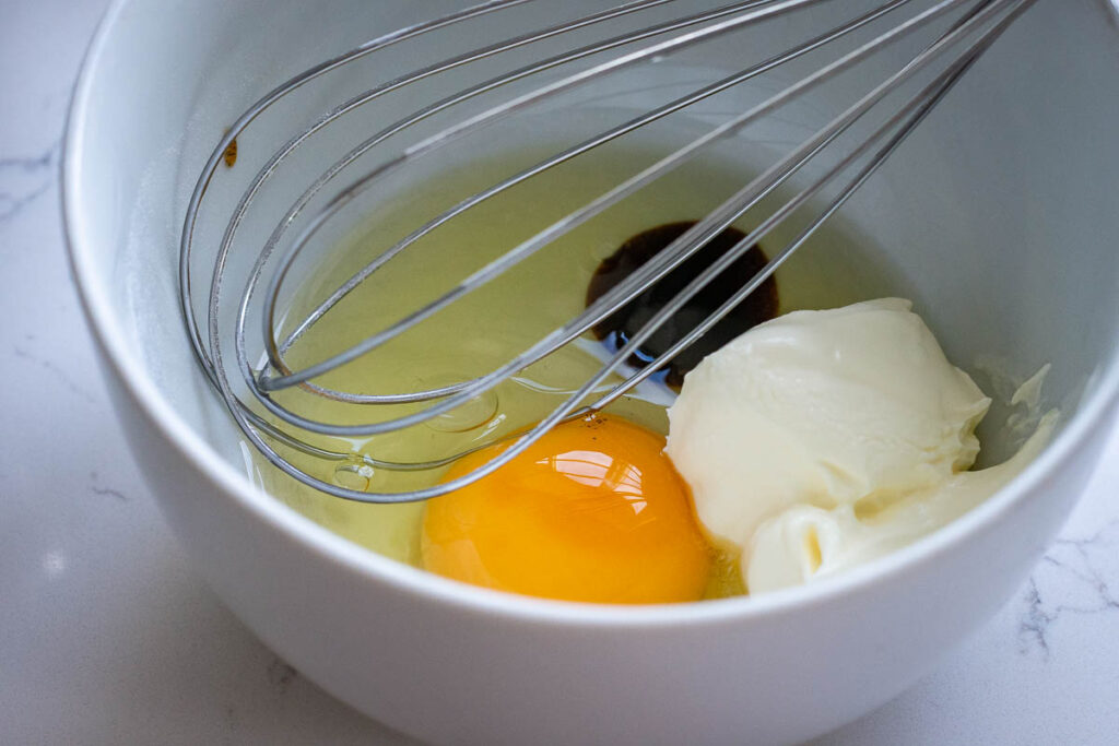 Wet ingredients in a small white bowl with a balloon whisk.