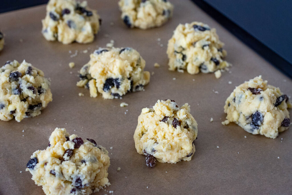 Mounds of crumbly roksai dough on a parchment paper lined baking sheet.