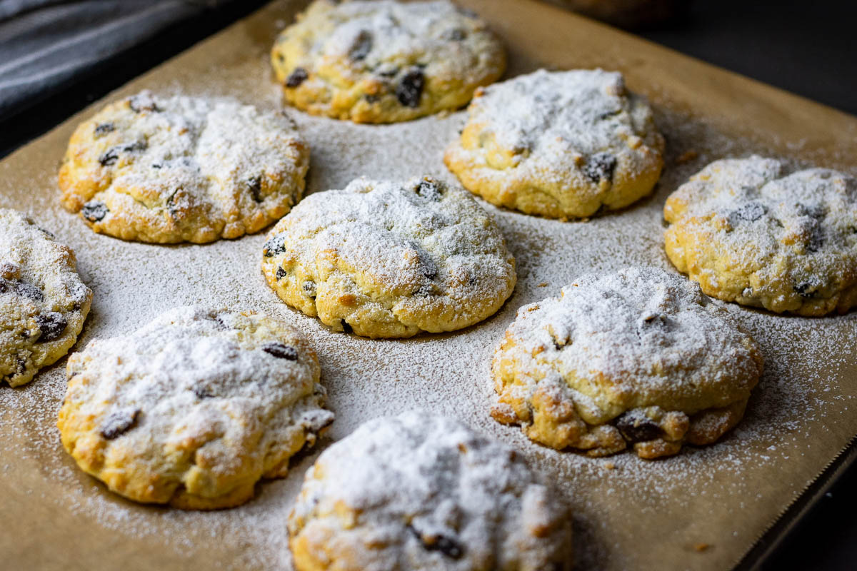 Rock cakes with raisins on a baking sheet lined with parchment paper dusted with powdered sugar.